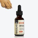bottle of resolvecbd's 600mg Bacon pet oil with a dog paw reaching for it