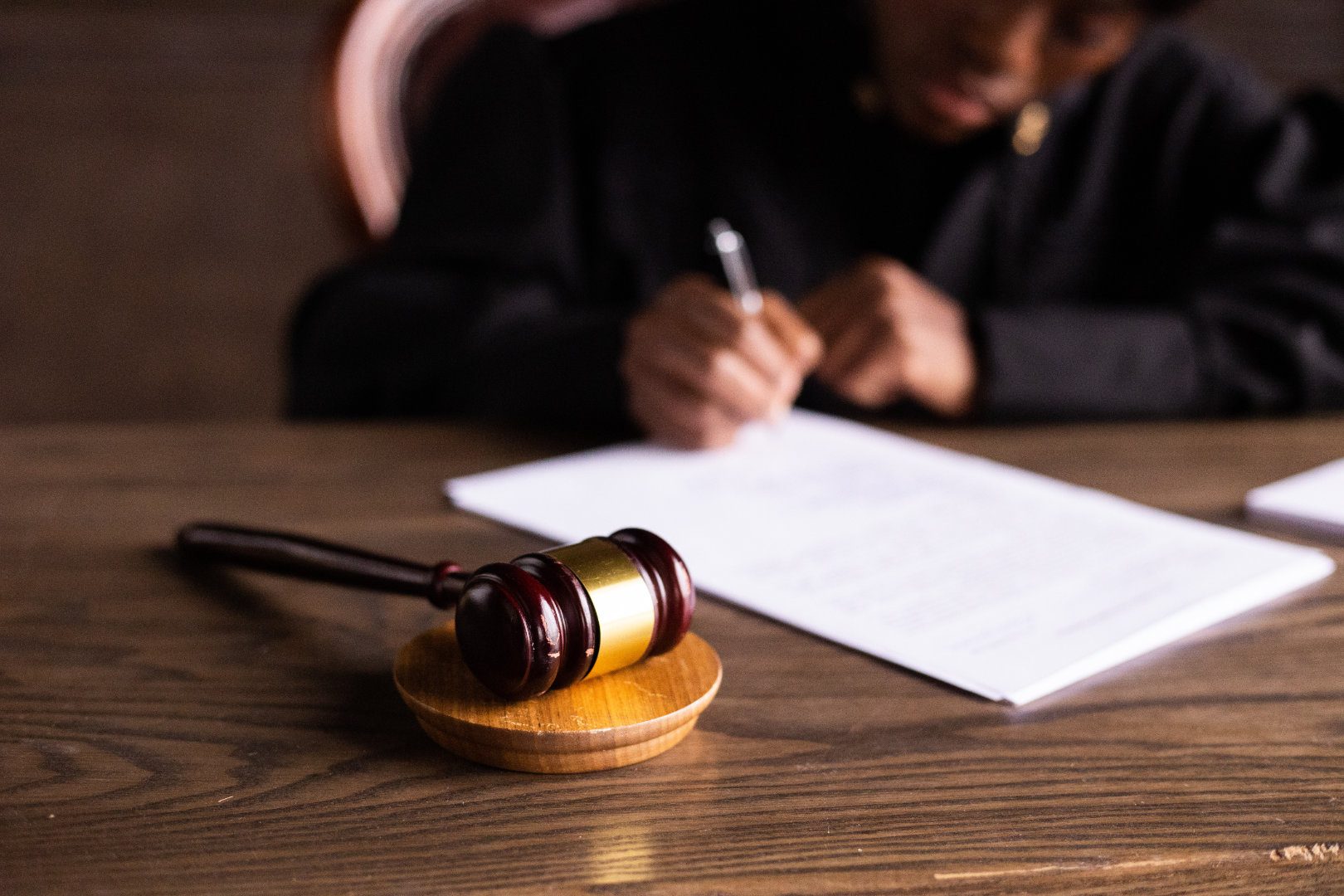 Person writing on a piece of paper with a gavel in the foreground