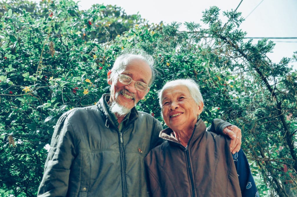 elderly couple smiling for a picture in from of a beautiful tree