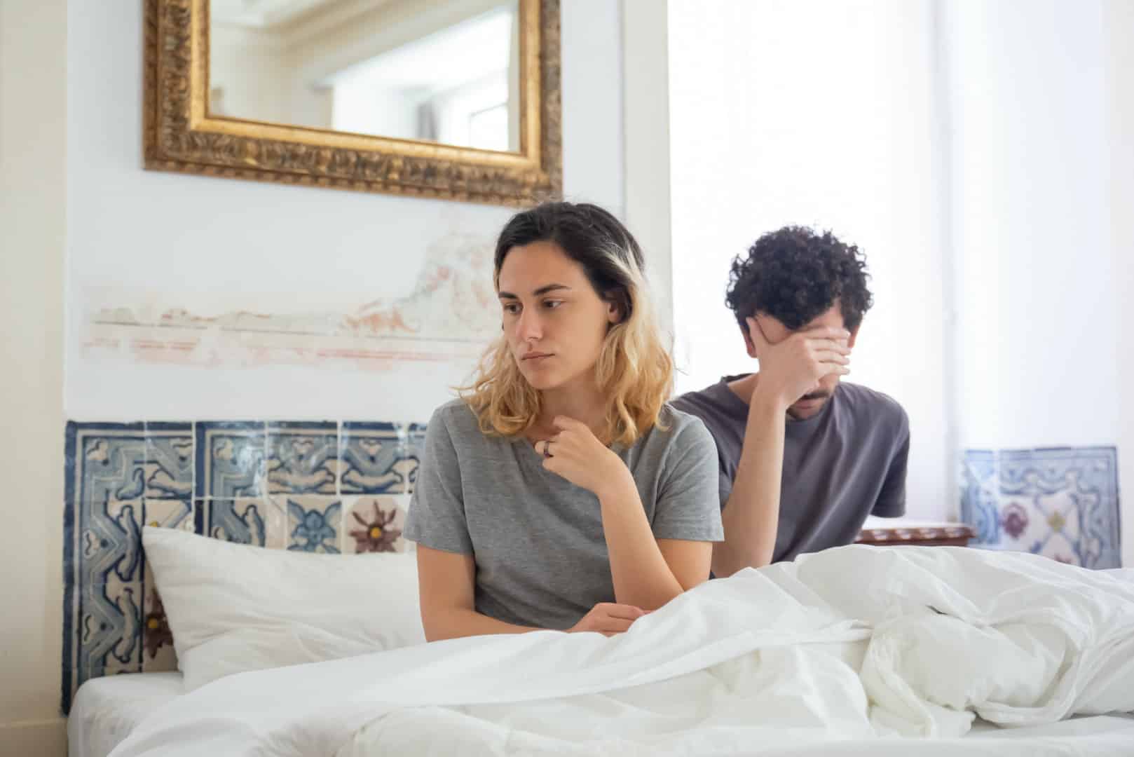 Couple sitting in bed and the man is embarassed