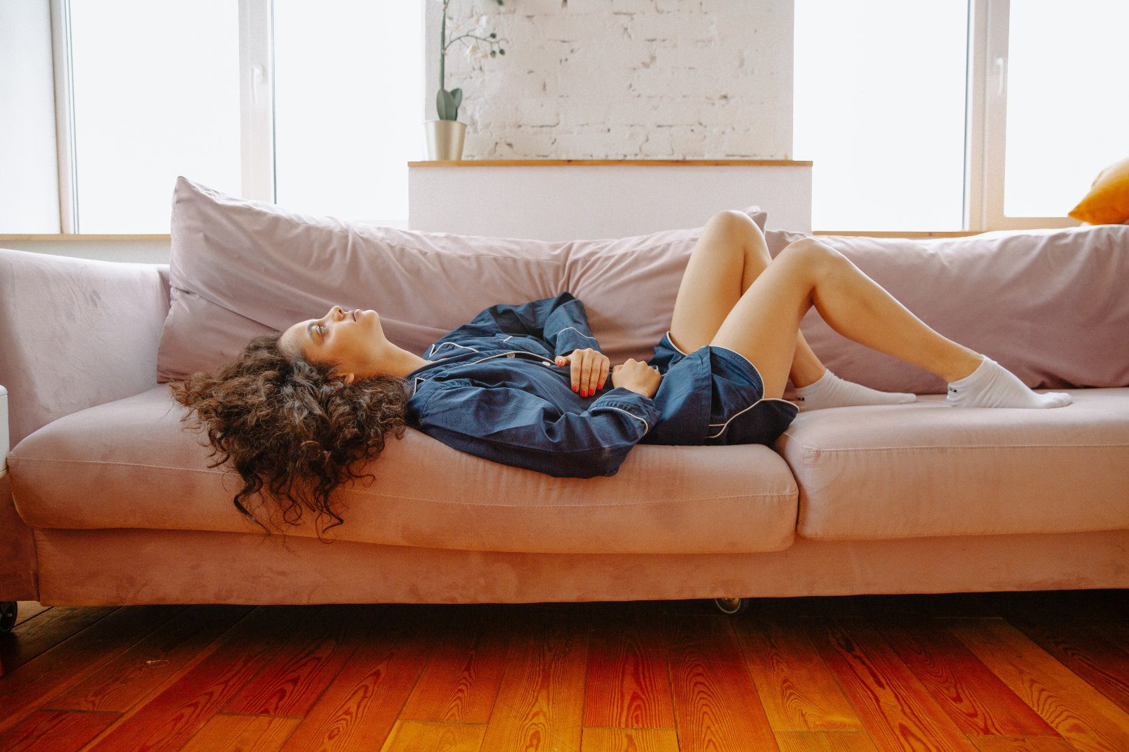 Woman laying down on couch holding stomach from stomach pain