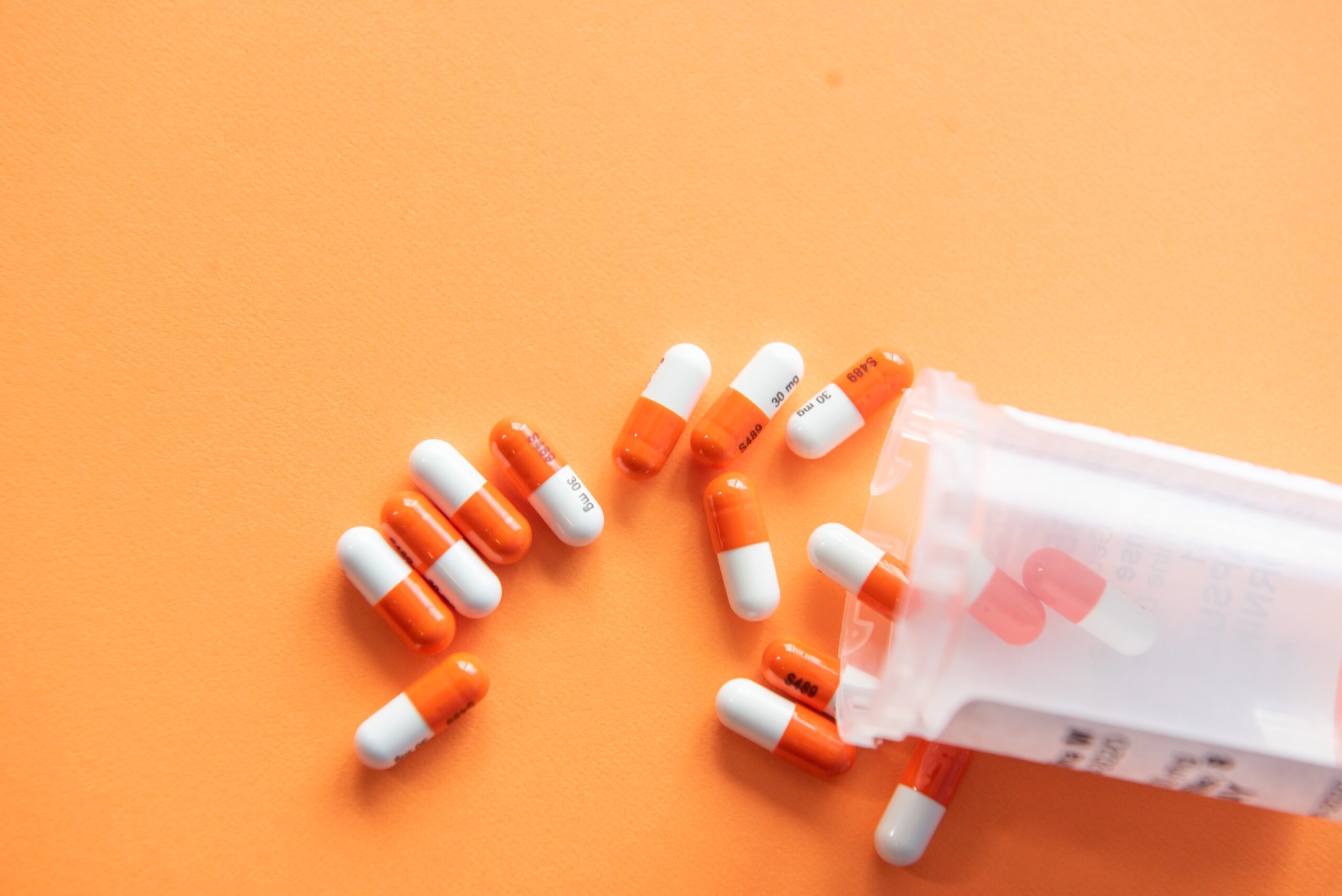 A bottle of orange & white pills spilling out of a medication container
