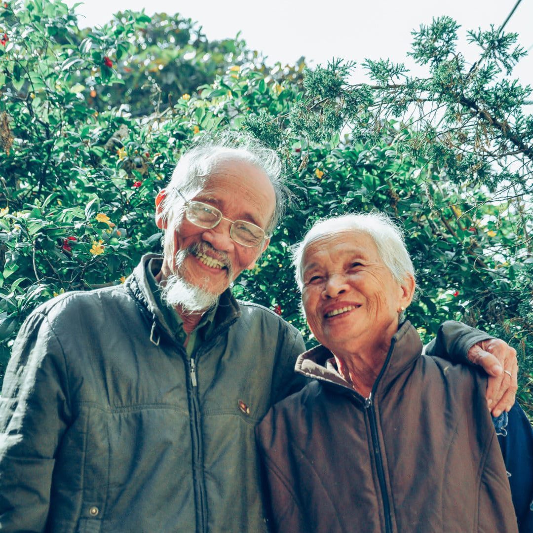 elderly couple smiling for a picture in from of a beautiful tree