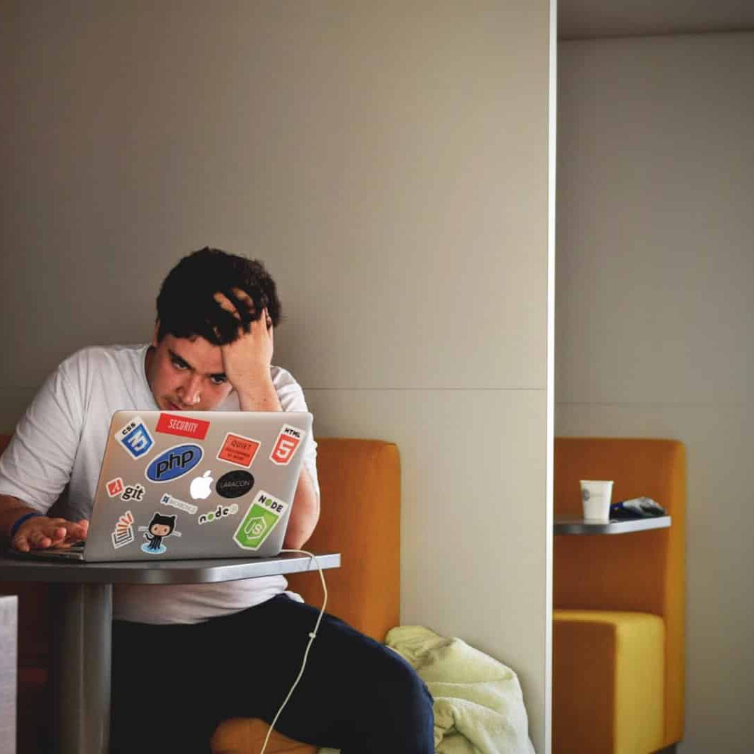 Student sitting down grabbing his head looking at is computer. He seems stressed